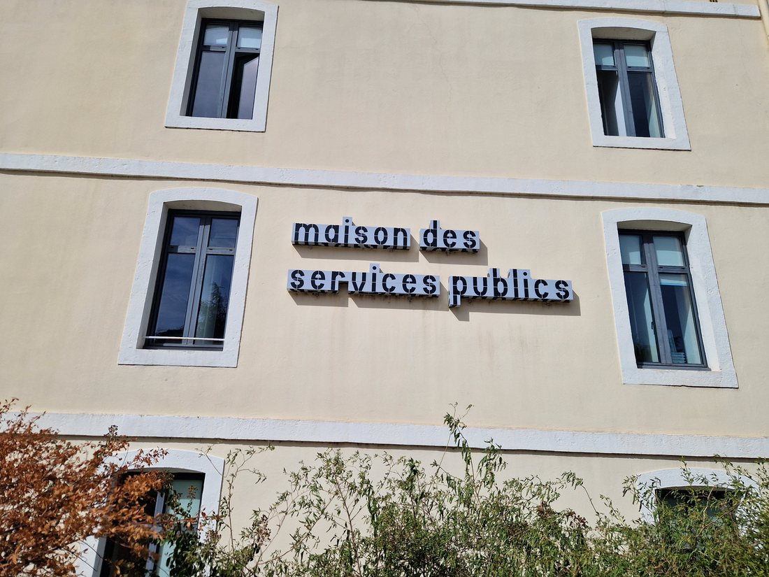 La façade de la Maison des services publics de Montélimar, mur jaune pâle avec les lettres découpées noir et blanc maison des services publics entre les fenêtres