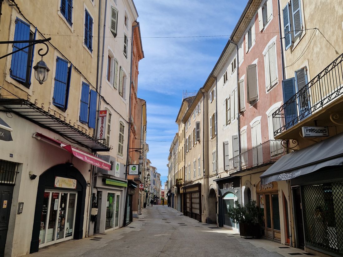 La rue Pierre Julien à Montélimar, rue piétonne bordée de façades ocre et rose aux volets bleus et gris, avec des boutiques en rez-de-chaussée